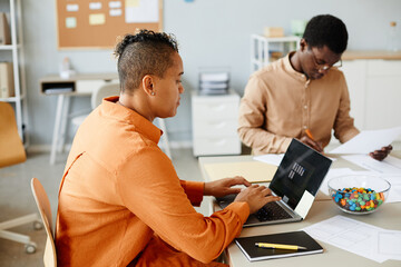Side view portrait of creative black woman using laptop while working with team in meeting