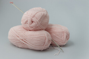Three skeins of pale pink yarn and two knitting needles on a gray background. Side view.