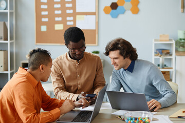 Creative business team of three using smartphone in meeting while developing mobile apps
