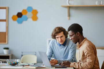 Side view portrait of two software developers using laptop together while working on project in IT...