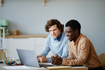 Minimal portrait of two young men using laptop together while working on project in software...