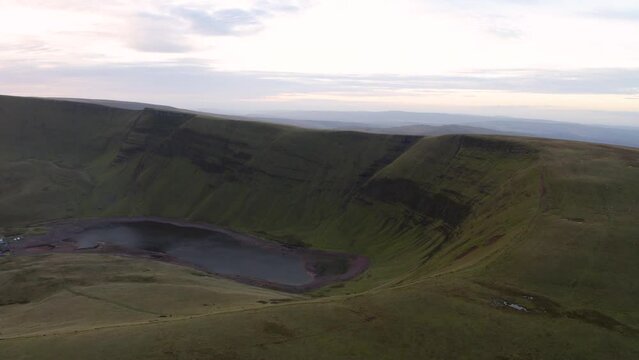 Aerial view of a lake at the foot of large cliffs (Llyn y Fan Fach). Idyllic Brecon beacons national park llyn y fan fach mountain range aerial.  Brecon Beacons National Park in Wales. 