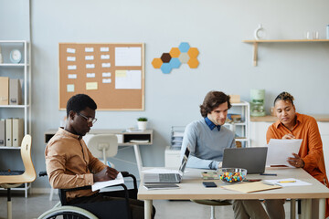 Side view portrait of black young man with disability working in office during diverse business team meeting