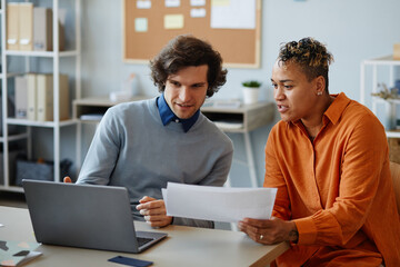 Portrait of two business people using laptop together while collaborating on project in minimal...