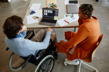 Top view of young man with disability talking to colleague or manager while working in IT...
