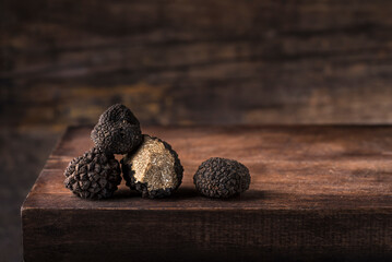 Black truffles in antique  wooden board, rustic style, low key, selective focus, macro, copy space for text. Season of black truffle. Autumn gourmet cuisine of Piedmont,  Italy, Spain and France