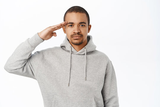 Image Of Young Man Saluting, Holding Hand Near Forehead, Army Greeting, Standing Over White Background