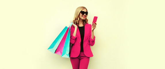 Portrait of happy smiling young woman with smartphone and shopping bags wearing business blazer on background