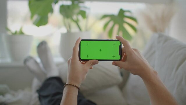 Man relaxing on couch interacting with phone, landscape, green screen mockup