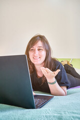 Vertical closeup of the woman with a laptop lying on the bed looking at the screen. Online chat.