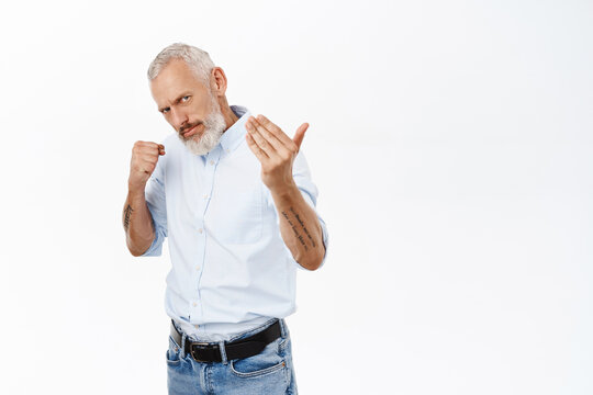 Image of serious senior man in shirt, clench fist and lure to come closer, fighting, standing over white background