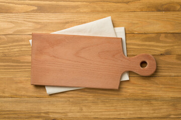 Cutting board with towel on wooden background, top view
