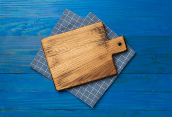 Cutting board with towel on wooden background, top view
