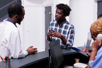 Fototapeta premium African american patient and doctor talking about disease diagnosis at hospital reception counter. Young adult and physician doing checkup consultation with medical appointment in clinic lobby.