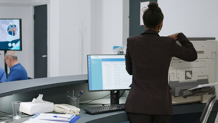 African american receptionist working at clinic registration desk with medical reports and checkup papers to help with appointments. Hospital worker giving insurance support at facility.