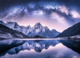 Milky Way arch over snowy mountains and lake at night. Landscape with snow covered high rocks,...