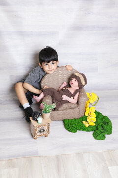 two sibling children playful face expression, cute infant boy wearing brown knitted dress head cap