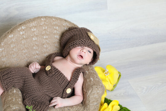 cute infant boy wearing brown knitted dress with head cap lying at tiny chair,face photography,props