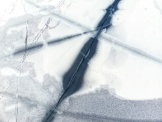Aerial drone top view of snow covered frozen lake or river surface with big cracked ice diagonal...