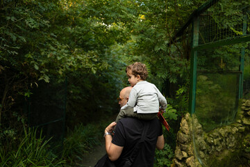 Niño a hombros de su padre paseando entre arboles al aire libre