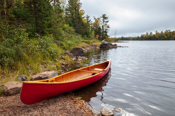Red wooden canoe on the shore of a northern Minnesota lake on an overcast autumn day