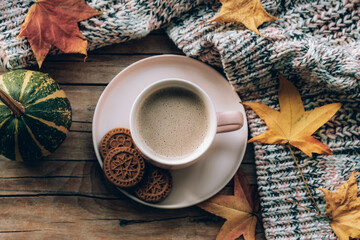 Coffee cup with cookies, pumpkin, autumn leaves and knitted sweater on wooden table. Fall concept....