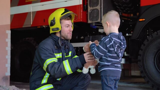 Brave firefighter in uniform and little boy with a toy against the background of a fire engine