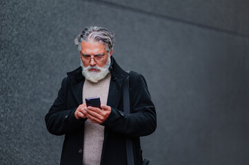 Portrait of a senior businessman using smartphone outside of the office building