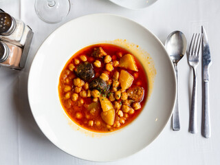 Spanish cuisine, chickpea shepherd soup with potatoes and sausages on a ceramic plate in restaurant