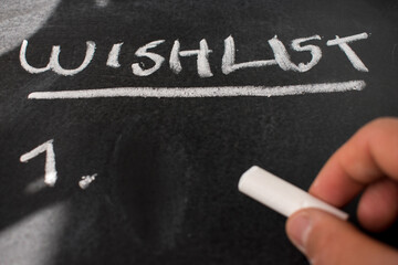 Hand writting a wishlist with white chalk on blackboard