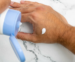A man's hand with moisturizing cream and a blue tube containing the product. Mention men's skin care and health, vanity and appearance for the day-to-day presentation of the body.