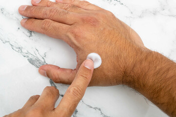 A man's hand spreading moisturizing cream over part of his hand. Mention the care of men's skin and...