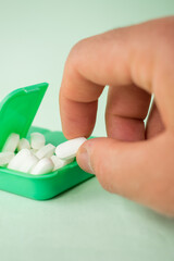 Hand taking a pill from some pills in a green pillbox on green background