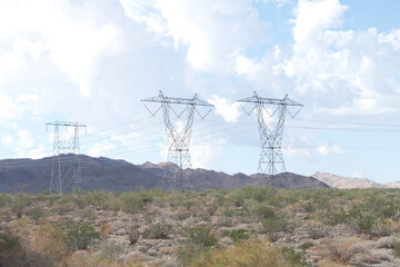 Large tall power lines running through desert landscape with mountains in the background. Blue skies with white clouds.