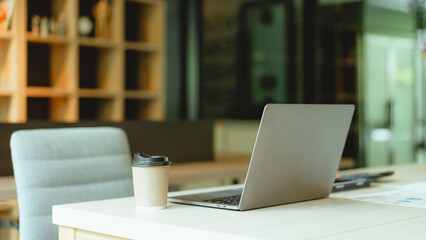 Modern workspace laptop and notebook on white table with blurred office room background.