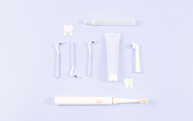 A set of small toothbrushes, toothpaste, an electric toothbrush and paper teeth on soft lilac.
