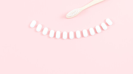 A bamboo toothbrush and chewing gums in a smile on a soft pink