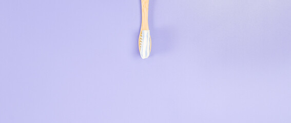 Bamboo toothbrush with toothpaste in the center on a soft lilac background