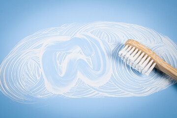 Bamboo toothbrush with smeared toothpaste and a painted tooth on a soft blue background