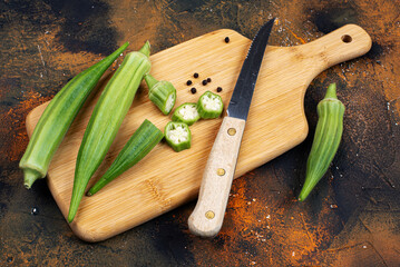 Okra on a cutting board with a knife. Pieces and whole pods. Abelmoschus esculentus.