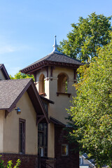 Close up architectural view of an early 20th century Spanish style church steeple and bell tower with stucco wall and arched windows