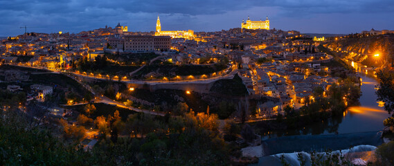 Scenic panoramic view of Spanish city of Toledo on banks of Tagus river overlooking illuminated medieval Alcazar fortress 