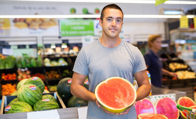 Satisfied male shopper holding watermelon in supermarket grocery section