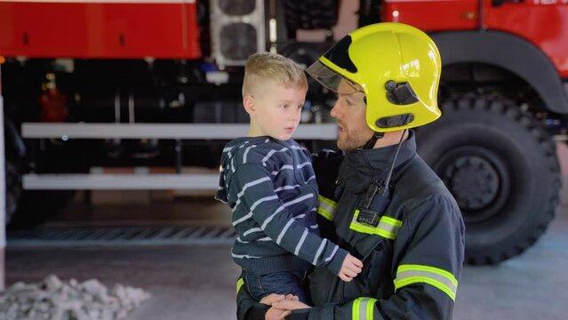 Portrait of firefighter with cute boy on arms. Concept of saving lives, fire safety
