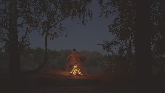 A shaman with a drum jumps in around the fire in clothes for the ceremony.