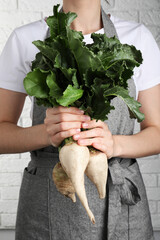 Woman holding sugar beets against white brick wall, closeup