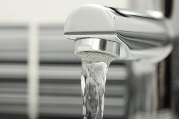 Water flowing from tap on blurred background, closeup. Space for text