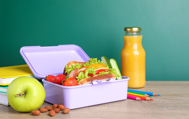 Lunch box with healthy food and different stationery on wooden table near green chalkboard