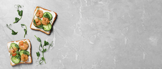 Tasty toasts with cream cheese, shrimps, cucumbers and microgreens on grey marble table, flat lay with space for text. Banner design