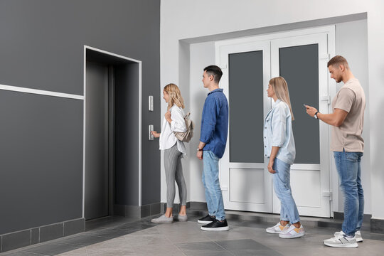 Group Of People Waiting In Line For Elevator While Woman Pressing Call Button